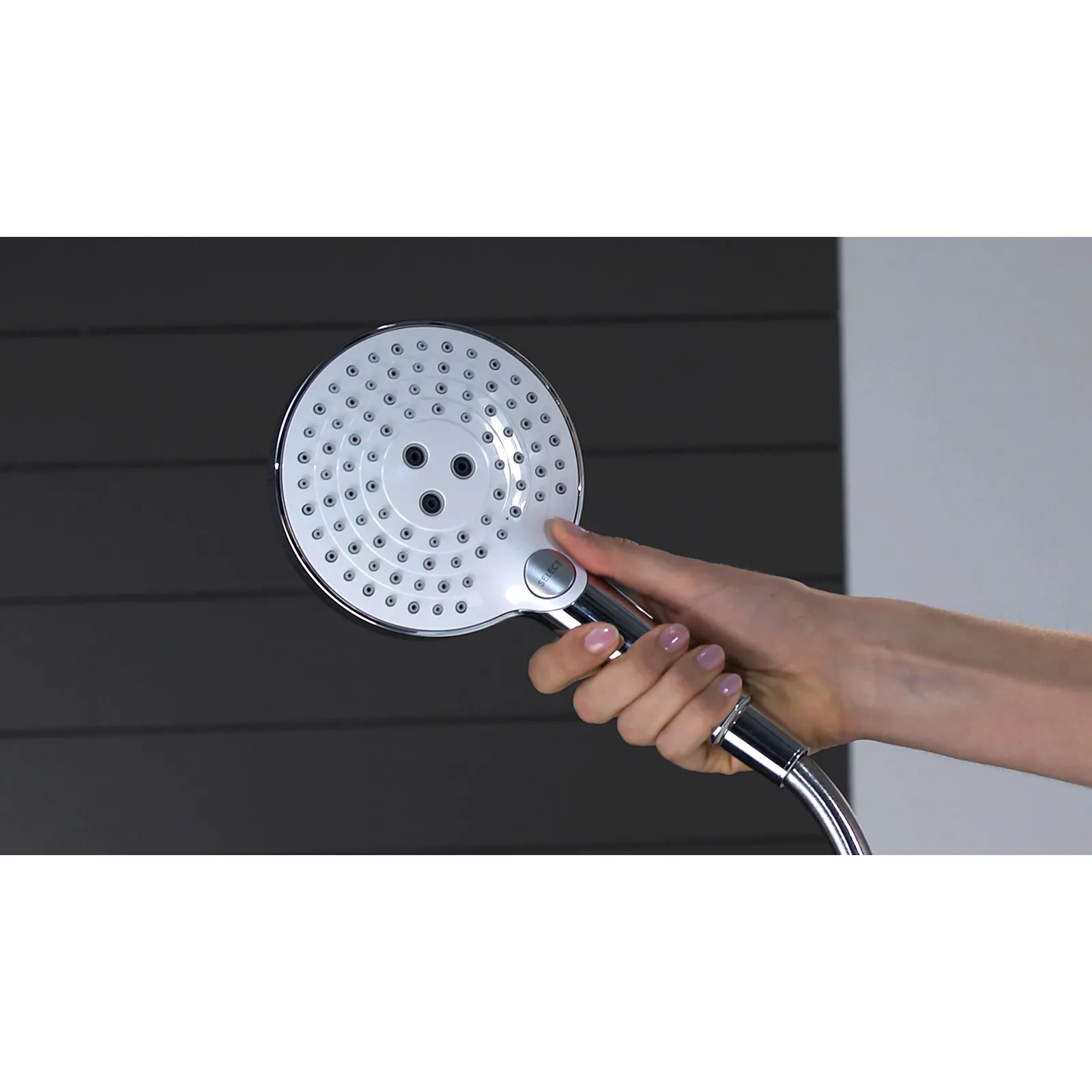 Eine Hand hält einen runden, glänzenden Duschkopf mit vielen kleinen Löchern. Der Duschkopf hat einen eleganten, metallischen Griff und ist vor einem dunklen Hintergrund präsentiert.