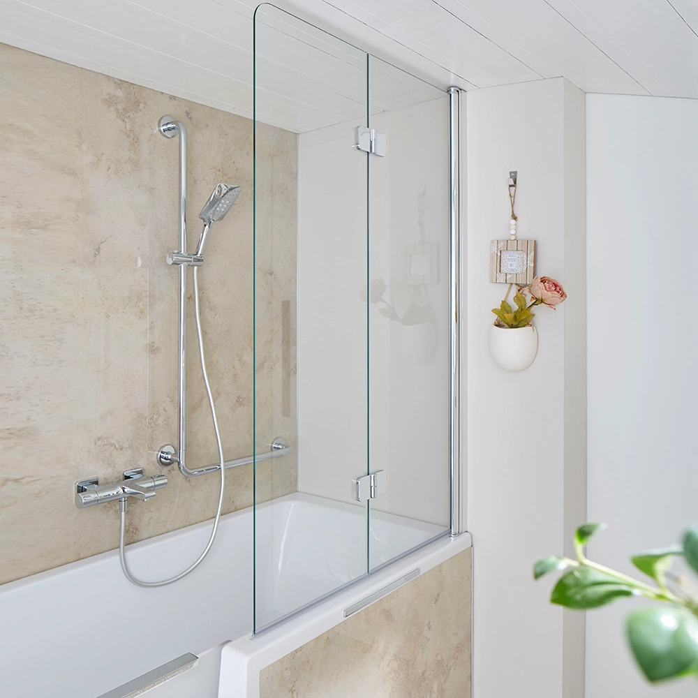 Ein Duschbereich mit einer transparenten Glasabtrennung, Chromarmaturen und einem modernen Badewannenrand. Die Wand ist in einem warmen Erdtone gehalten, mit einer minimalen Dekoration aus einer Blume.