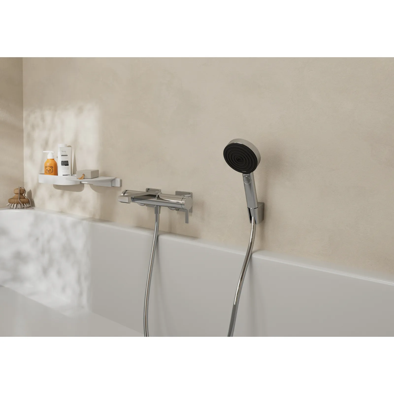 Eine chromfarbene Badewannenarmatur mit einer Handbrause ist an einer beige Wand montiert. Neben der Armatur befindet sich ein schwebendes Regal mit Pflegeprodukten. Die Badewanne ist weiß und schlicht.