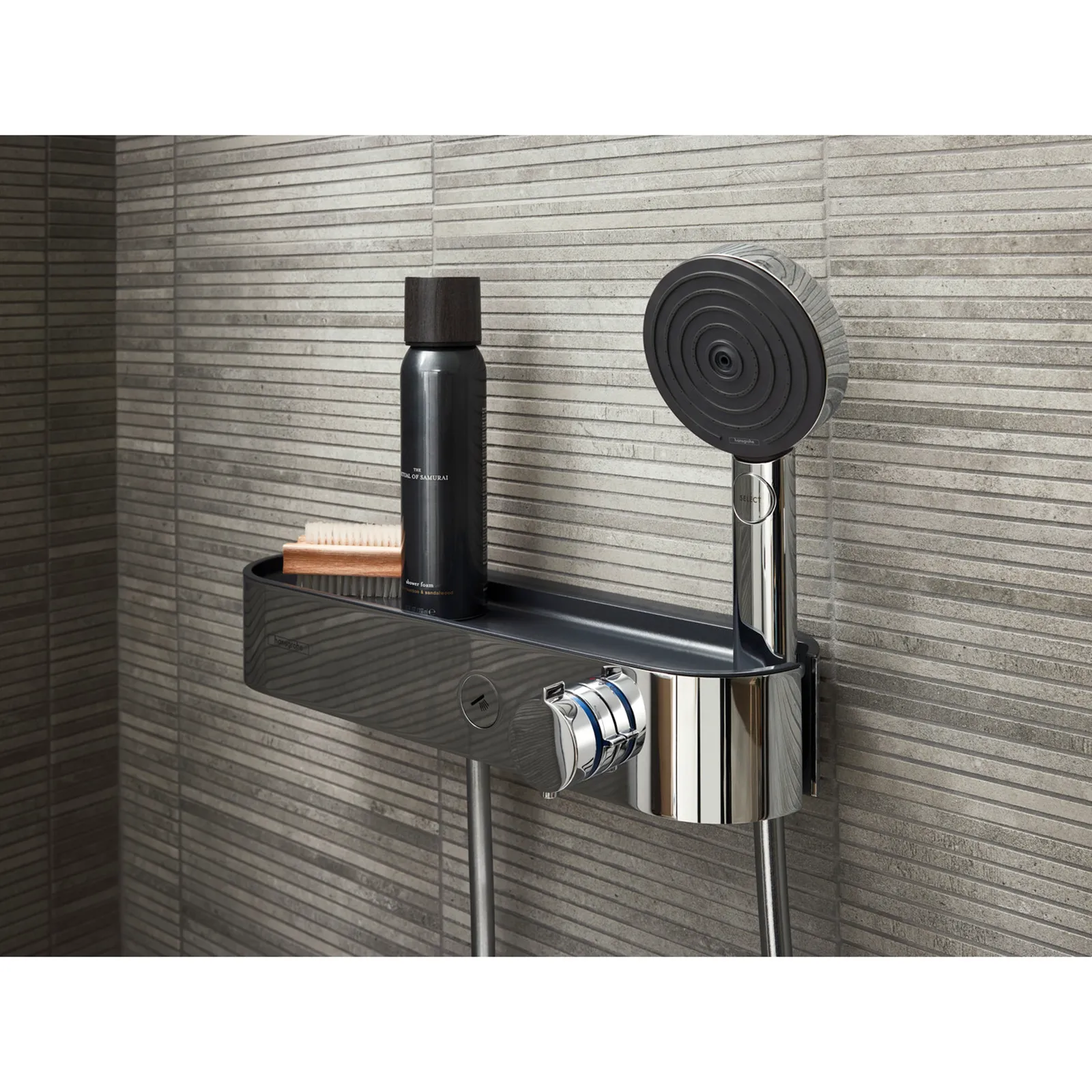 Eine Dusche mit einer modernen Handbrause, die auf einem eleganten, glänzenden Halter montiert ist. Der Halter bietet Platz für Shampoo und einen Kamm. Der Hintergrund zeigt strukturierte graue Fliesen.