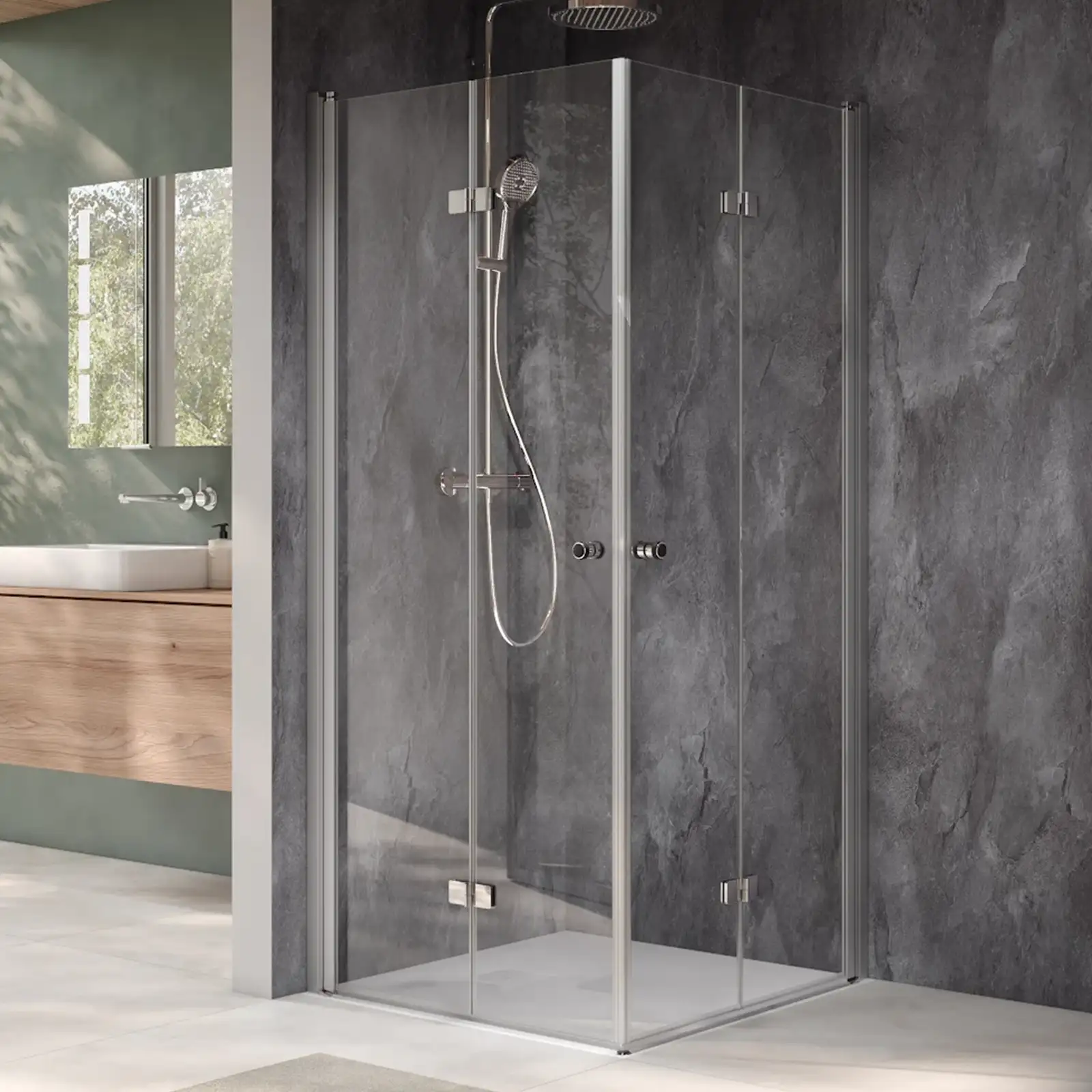 Eine moderne Duschkabine aus klarem Glas mit silbernen Profilen. Die Dusche hat einen Handbrausekopf und ist vor einer grauen Wand in einem eleganten Badezimmer platziert, das viel Tageslicht erhält.