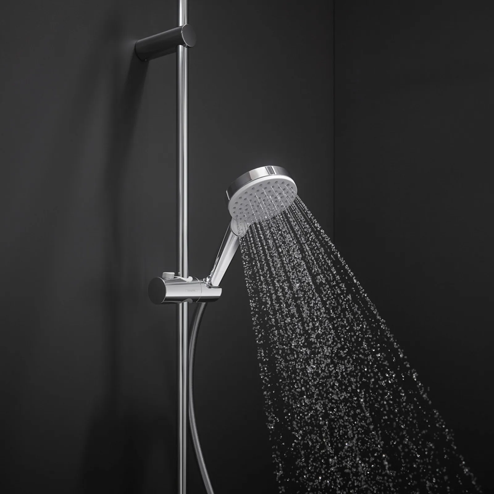 Ein verchromter Duschkopf sprüht Wasserstrahlen in einem modernen, minimalistischen Duschbereich, der von einer dunkeln Wand umgeben ist. Der Duschkopf ist an einer verchromten Halterung montiert.