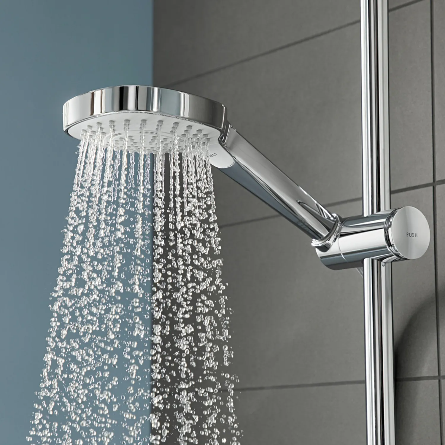 Die Duschbrause mit glänzendem Chromfinish ist rund und strahlt Wasser in feinen Strahlen aus. Im Hintergrund sind graue Fliesen zu sehen, die einen modernen Badezimmerkontext schaffen.