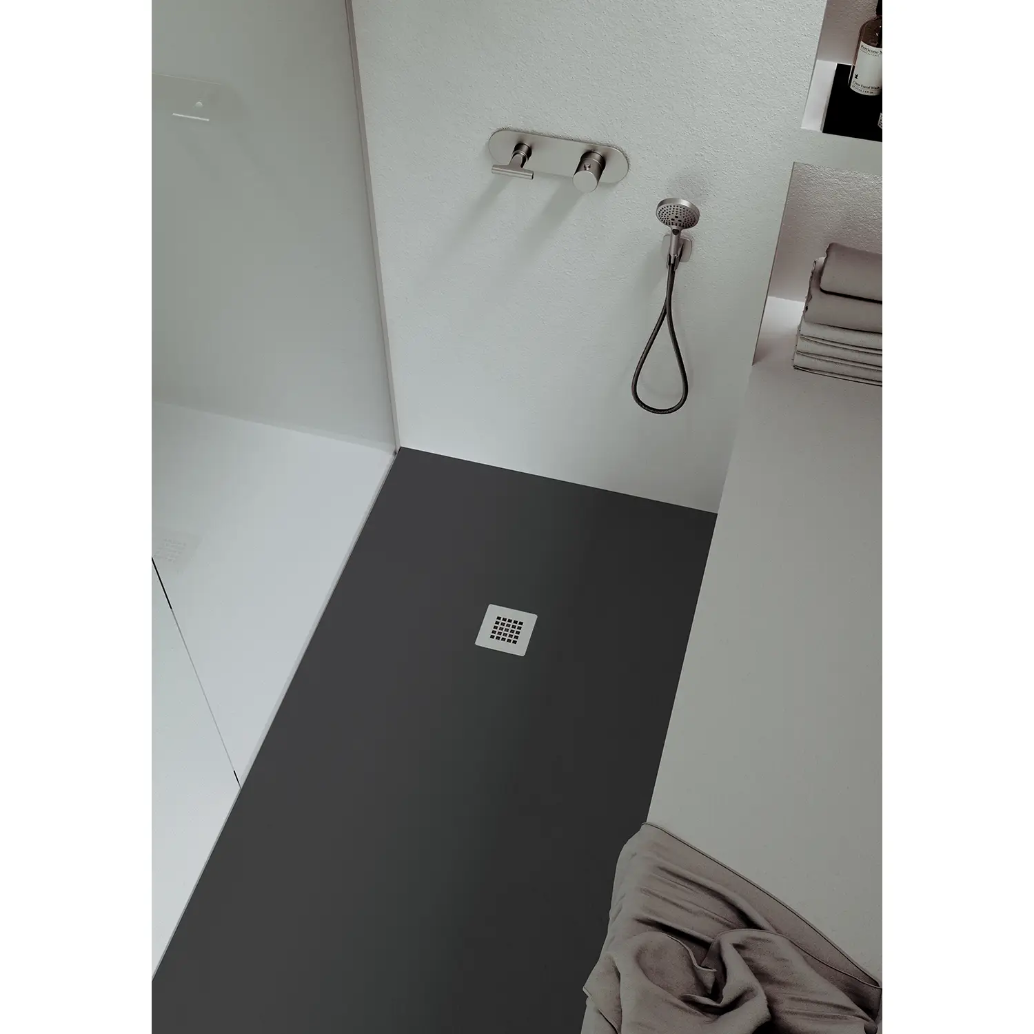 Eine moderne Dusche mit einem grauen Bodenbelag, einer seifenschonenden Armatur und einer Handbrause. Im Hintergrund sind Handtücher und ein Regal sichtbar, alles in einem minimalistischen Design.
