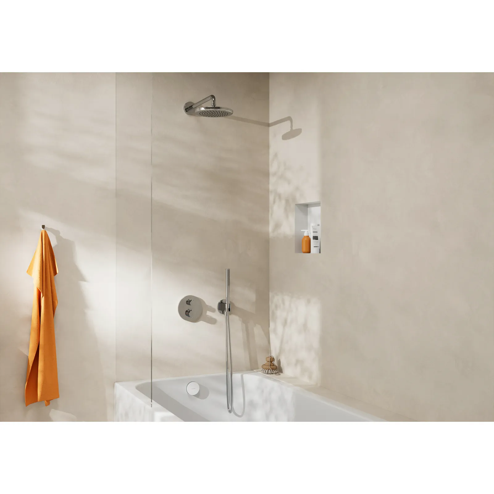 Ein Duschsystem mit einer großen Kopfbrause in Chromfarbe ist an einer glatten, hellen Wand installiert. Daneben befindet sich eine Badewanne mit einer Edelstahlarmatur und eine Nische für Pflegeprodukte. Ein oranger Handtuch hängt links.
